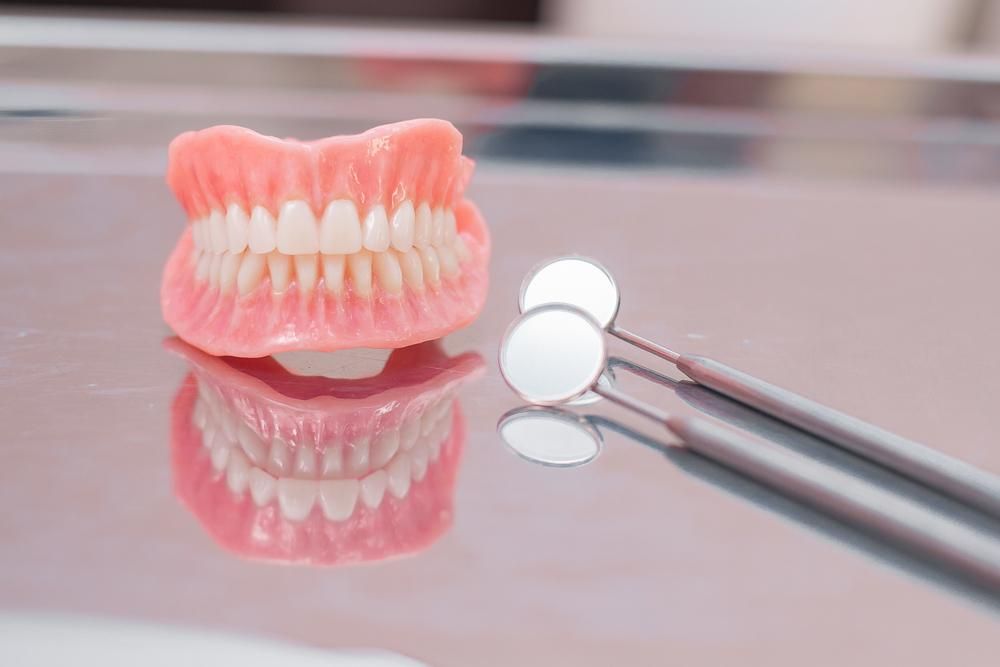A Denture Is Sitting on A Table Next to A Pair of Dental Mirrors — Cosmetic Denture Services–Jacob Maxwell in Moranbah, QLD