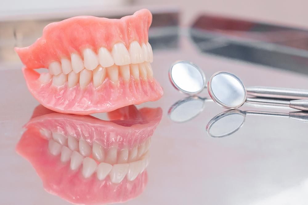 A Denture Is Sitting On A Table Next To A Pair Of Dental Mirrors — Cosmetic Denture Services–Jacob Maxwell in Sarina, QLD