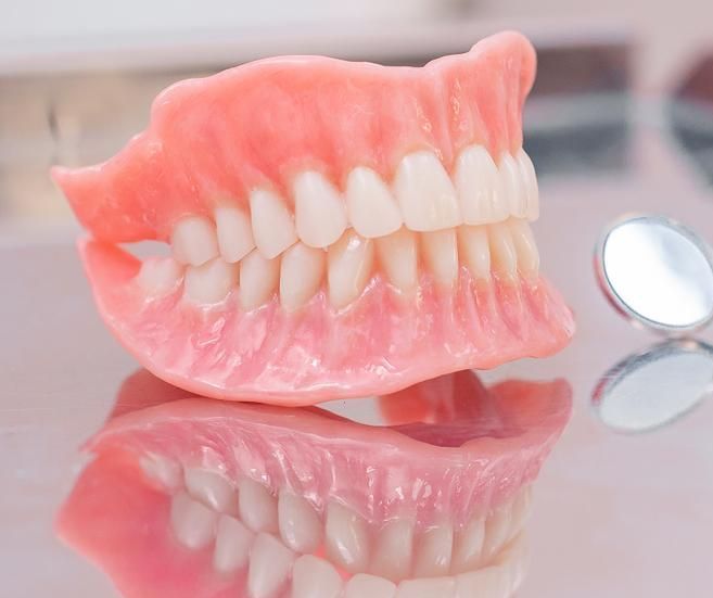 Denture is Sitting on a Table Next to a Dental Mirror — Cosmetic Denture Services–Jacob Maxwell in Mackay, QLD