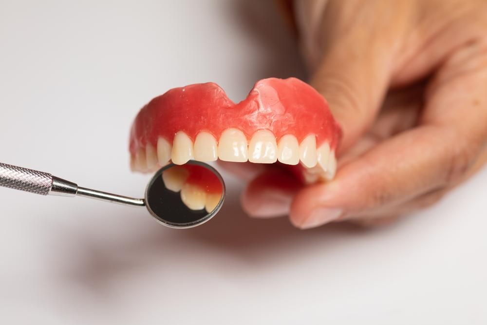 A Person Is Examining a Denture with A Dental Mirror — Cosmetic Denture Services–Jacob Maxwell in Proserpine, QLD