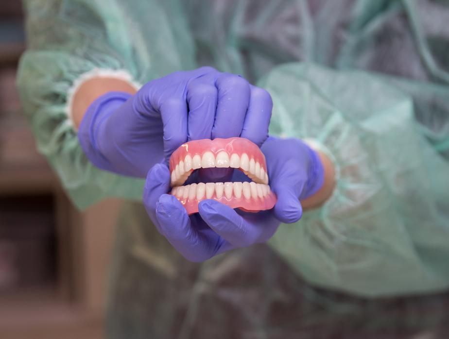 Person Wearing Purple Gloves is Holding a Denture in Their Hands — Cosmetic Denture Services–Jacob Maxwell in Mackay, QLD