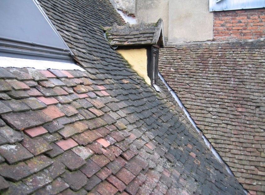 Rooftops with weathered gray and red tiles on a sloped, overlapping roofline