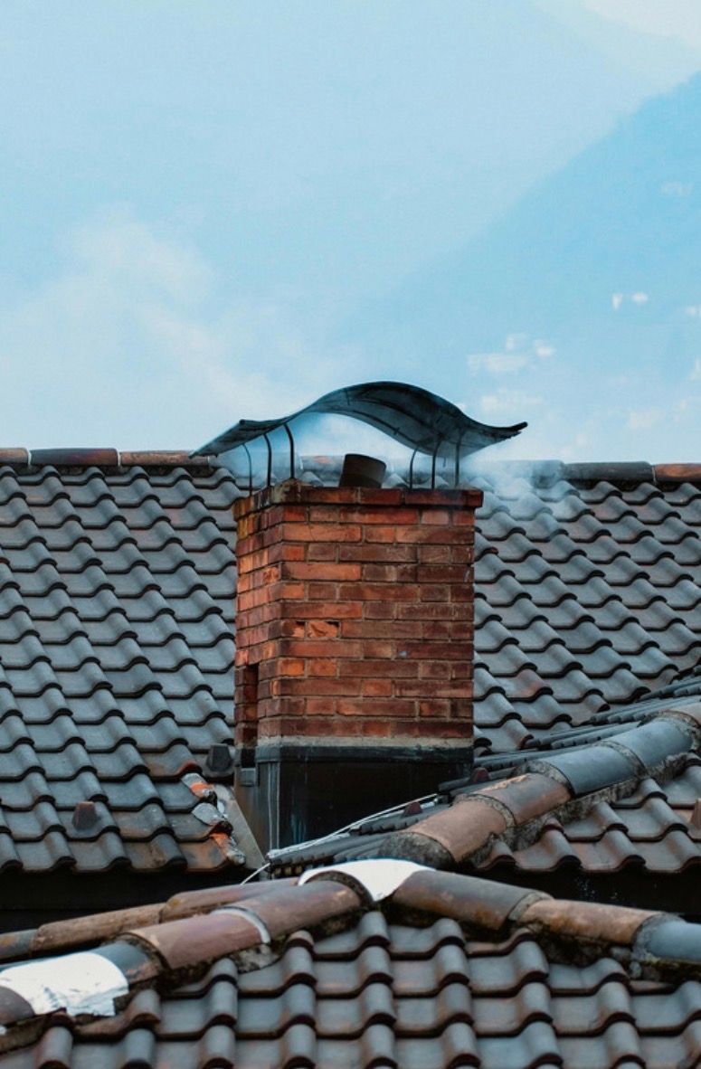 Black cat perched on a brick chimney above red-tiled rooftops under a blue sky