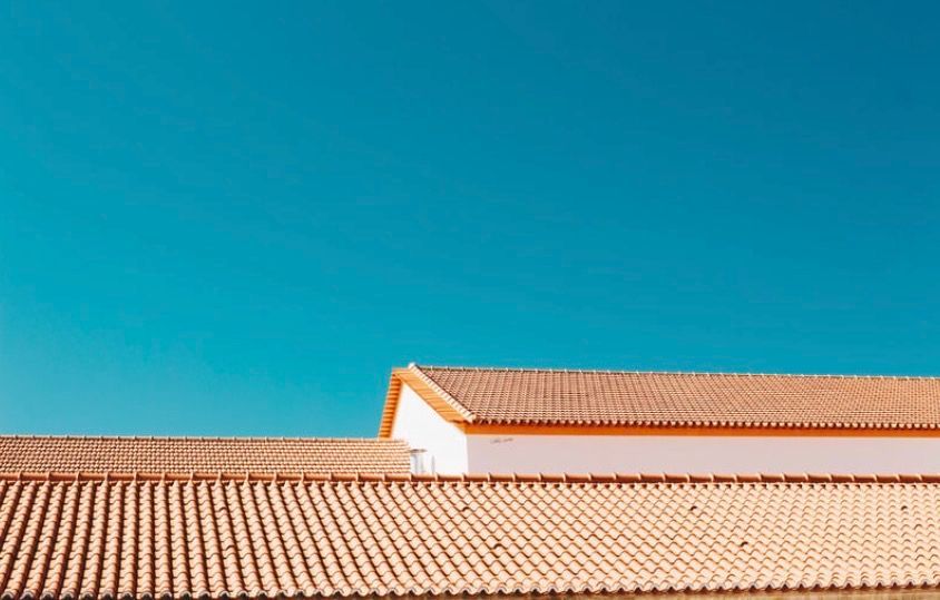 Terracotta roof tiles against a clear blue sky, with a white building edge visible above the roofline