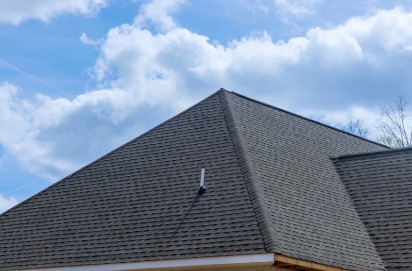 Dark gray shingled roof with a small vent under a blue cloudy sky