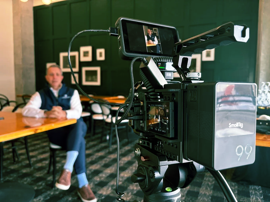 Video camera on tripod in a green cafe, with a seated person blurred in the background.