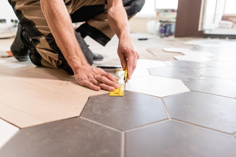 a Man is Kneeling on the Floor While Installing Tiles — Port Stephens Bathrooms In Nelson Bay, NSW