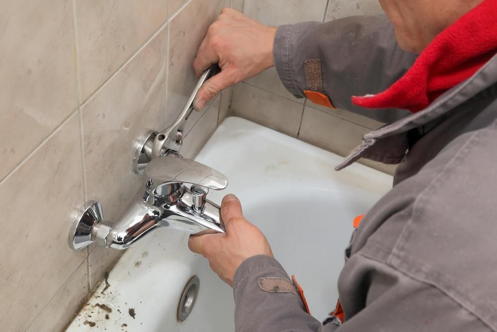 A Man Is Fixing A Bathtub Faucet With A Wrench — Port Stephens Bathrooms In Shoal Bay, NSW
