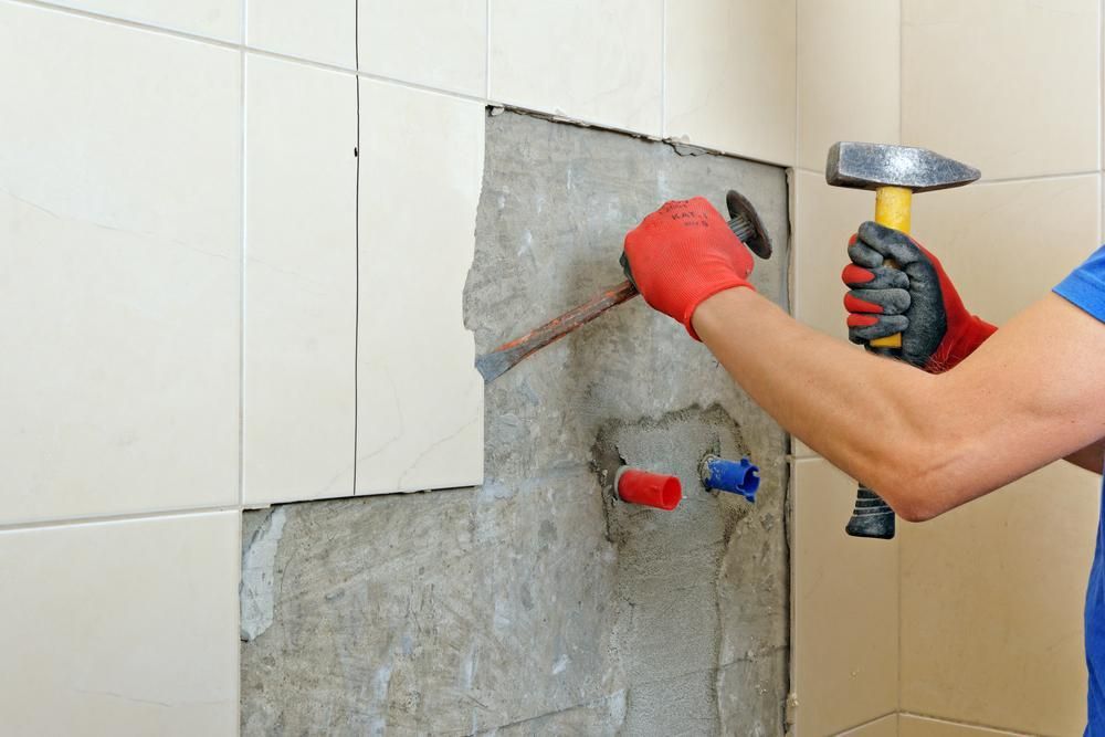 a Man is Using a Hammer to Remove Tiles From a Wall — Port Stephens Bathrooms In Nelson Bay, NSW