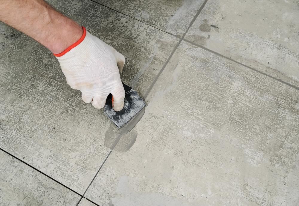 a Person is Using a Spatula to Repair a Tile Floor — Port Stephens Bathrooms In Newcastle, NSW