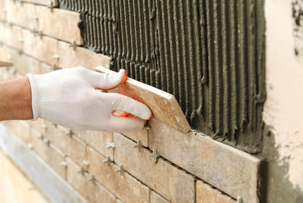 a Person is Laying Tiles on a Brick Wall — Port Stephens Bathrooms In Merewether, NSW