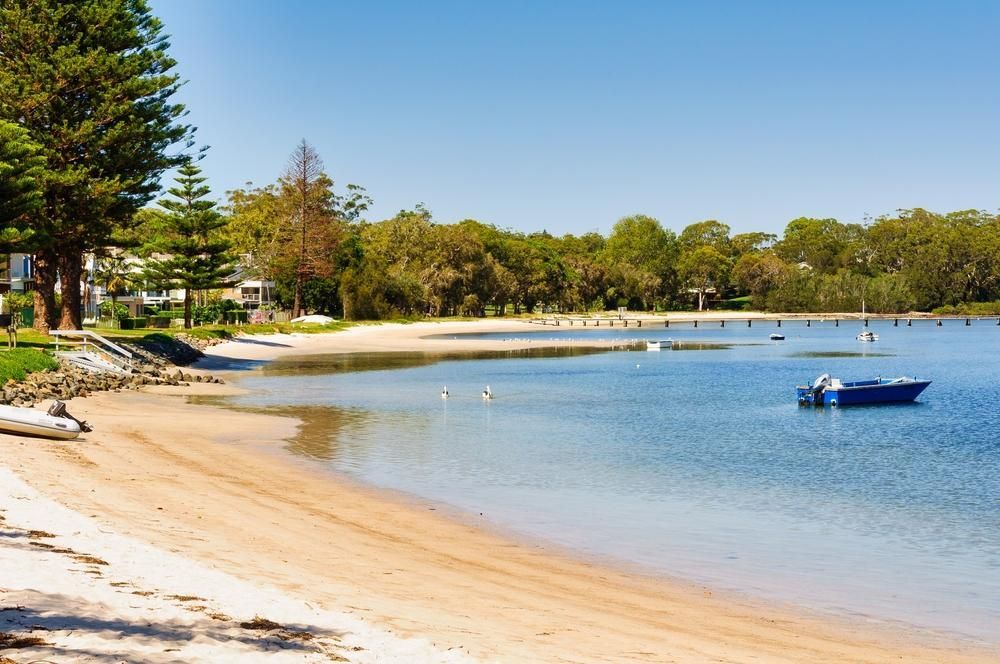 a Boat is Floating on the Water Near a Beach — Port Stephens Bathrooms In Soldiers Point, NSW