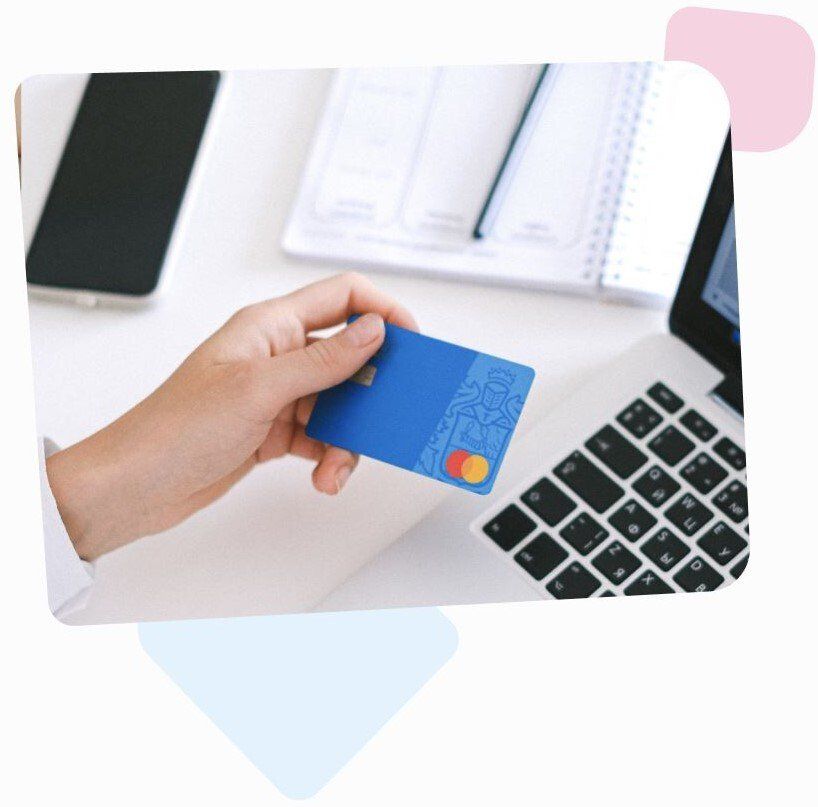hand holding a blue mastercard credit card above a laptop and a notebook