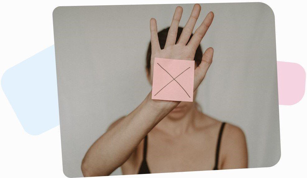 woman wearing a black tank top and covering her face with a pink square paper with black cross on it