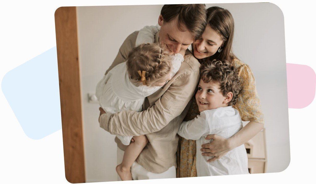 happy family of four with a hudband, wife and two little children hugging each other in their home
