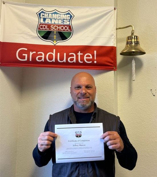 A man is standing in front of a truck holding a CDL certificate.