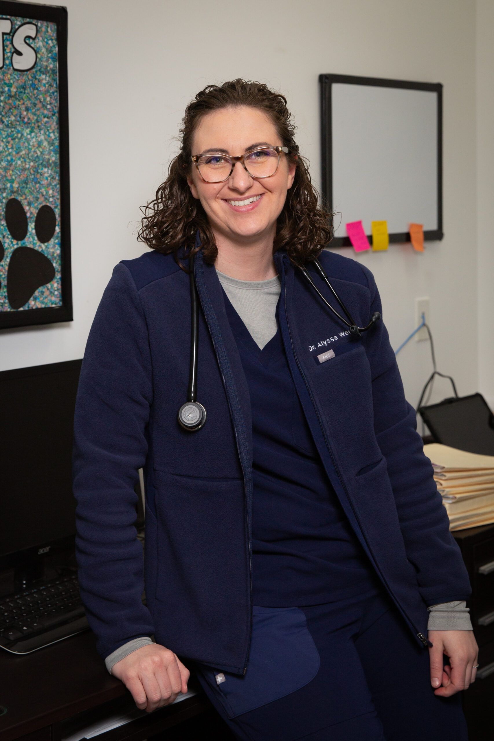 A woman wearing glasses and a stethoscope is standing in a room.