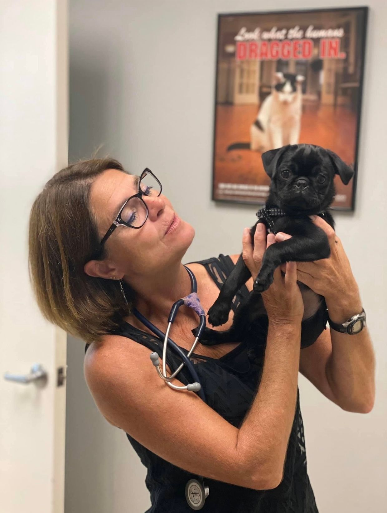 A woman is holding a small black dog in her arms