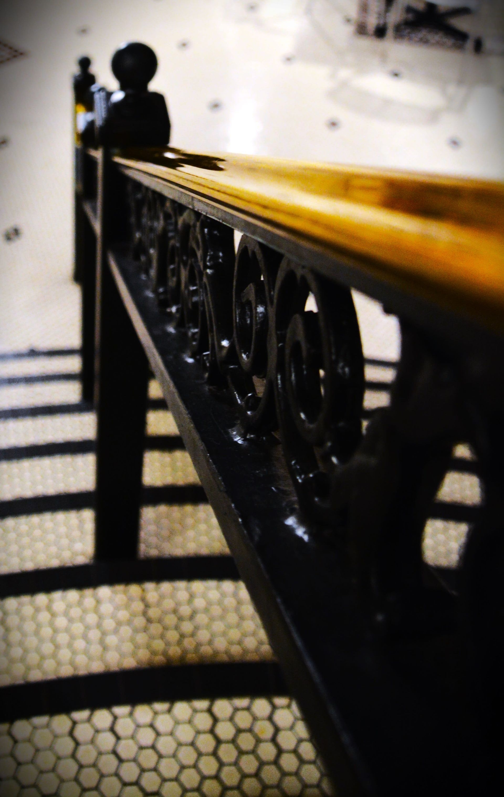 Black and gold ornate staircase handrail with shadow on patterned floor.