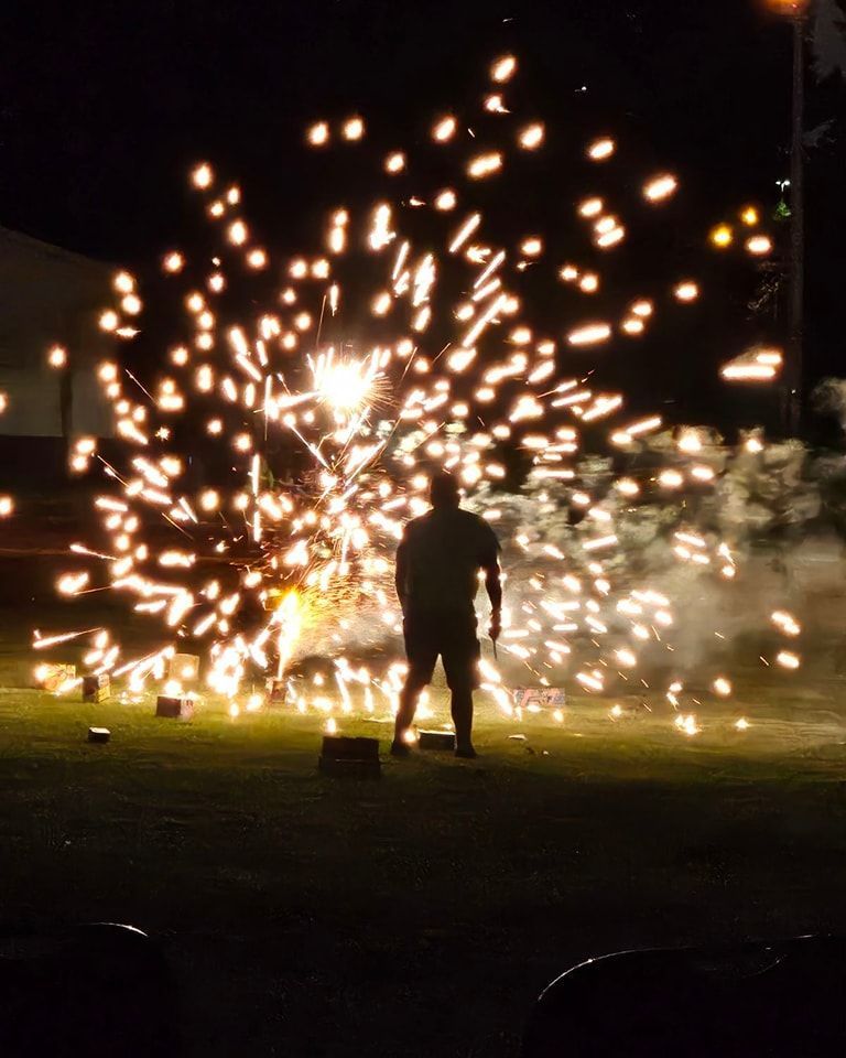 Person standing in front of exploding fireworks at night. Bright orange and white sparks burst outward.