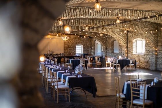 Interior of a stone-walled event space with tables, chairs, string lights, and arched ceilings.