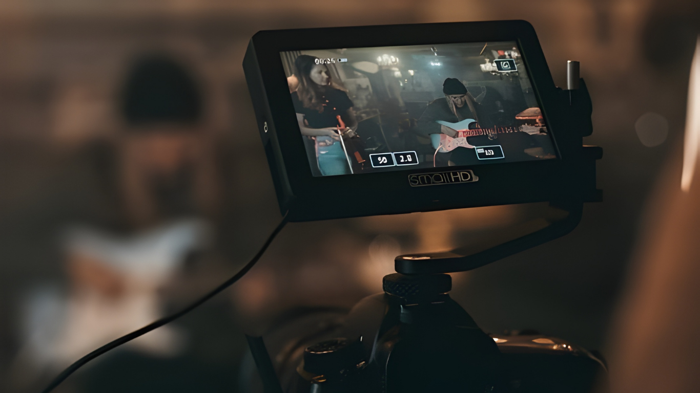 A camera monitor displays a band performing on stage. It's dark, with out-of-focus figures in the foreground.