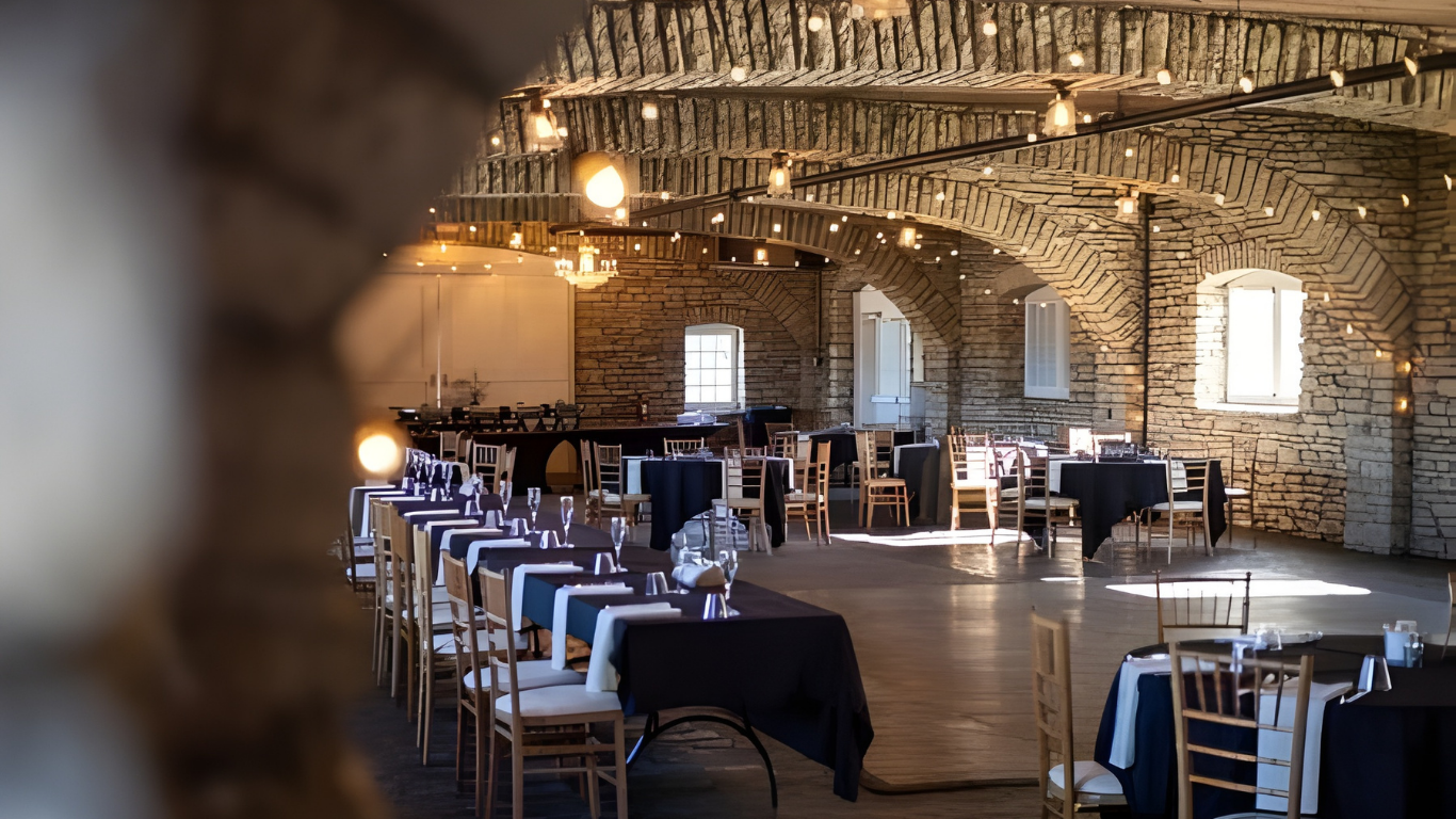 Stone-walled event space with tables set for a gathering, strung with decorative lights.