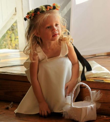 Young girl in white dress and floral crown, holding a basket.