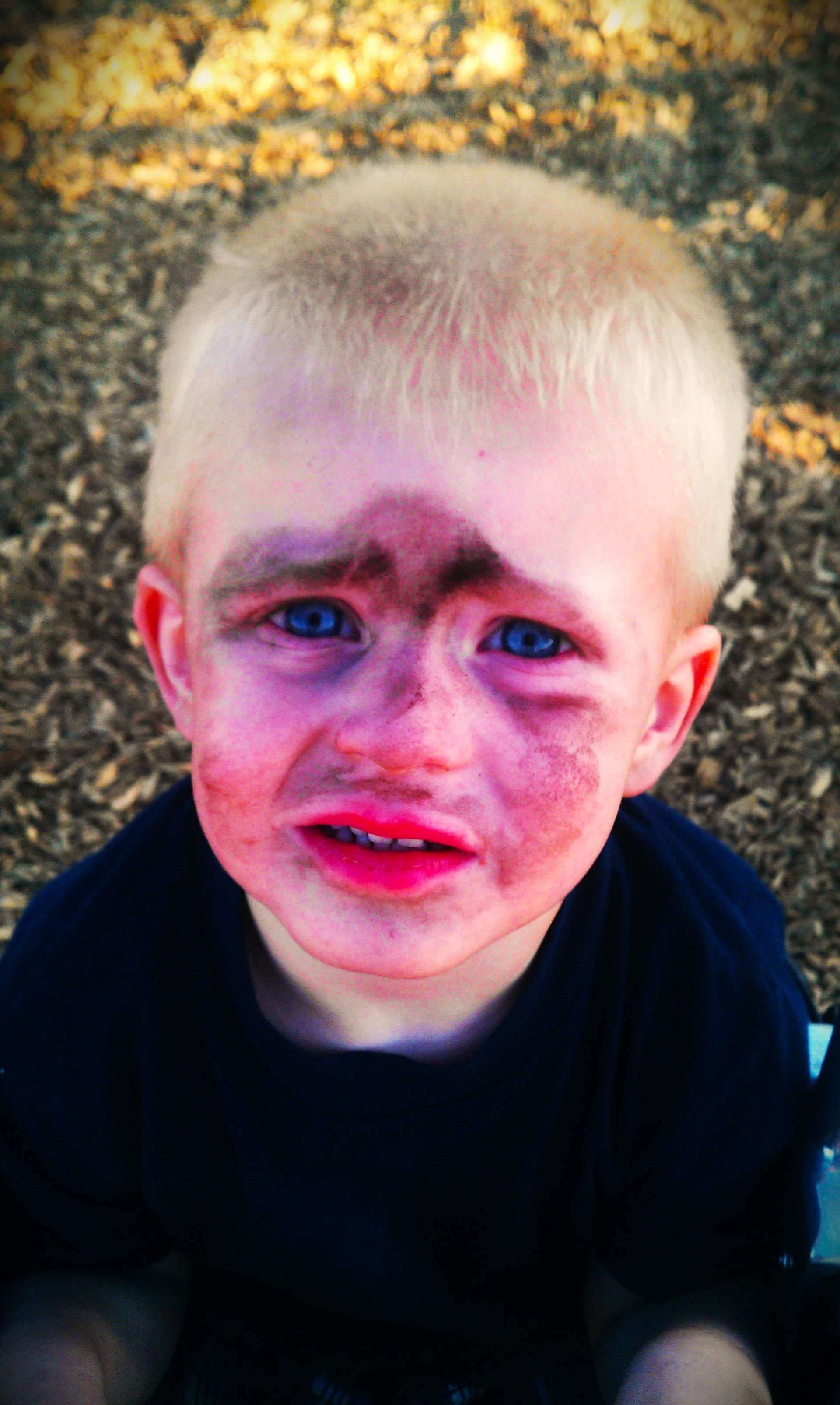 Blond child with tear-streaked, dirt-covered face. Looks upset with red lips and blue eyes.