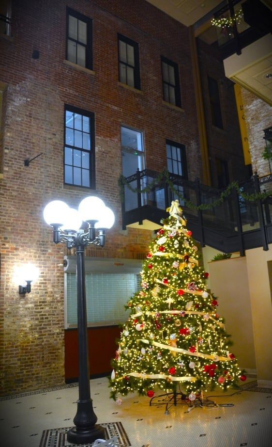 Lit Christmas tree in an indoor brick building with windows and a decorative lamppost.