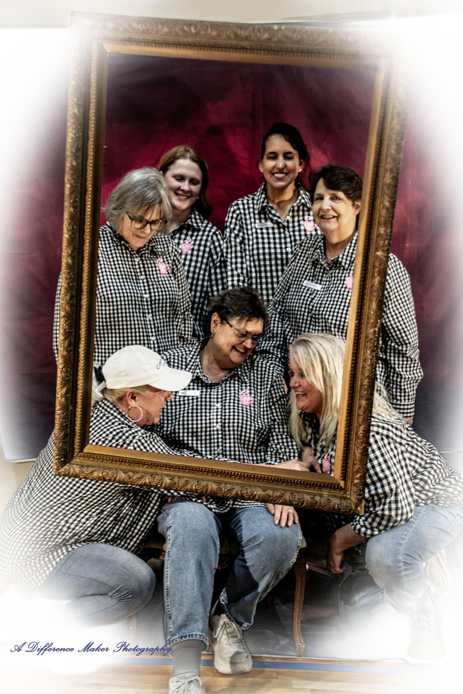 Group of people in matching checkered shirts framed by a gold picture frame, smiling.