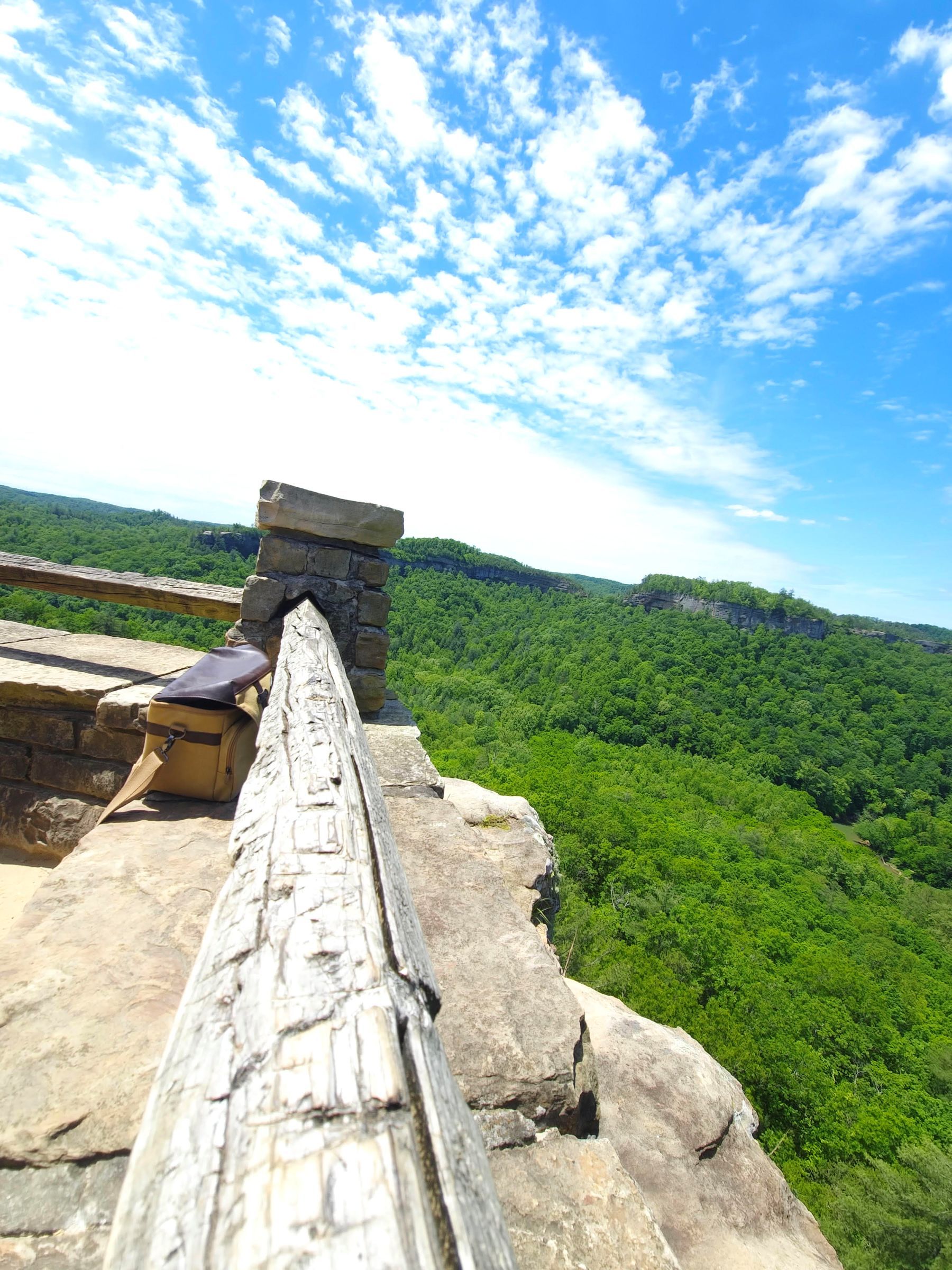Stone railing overlooking lush green forest under a blue sky with clouds.