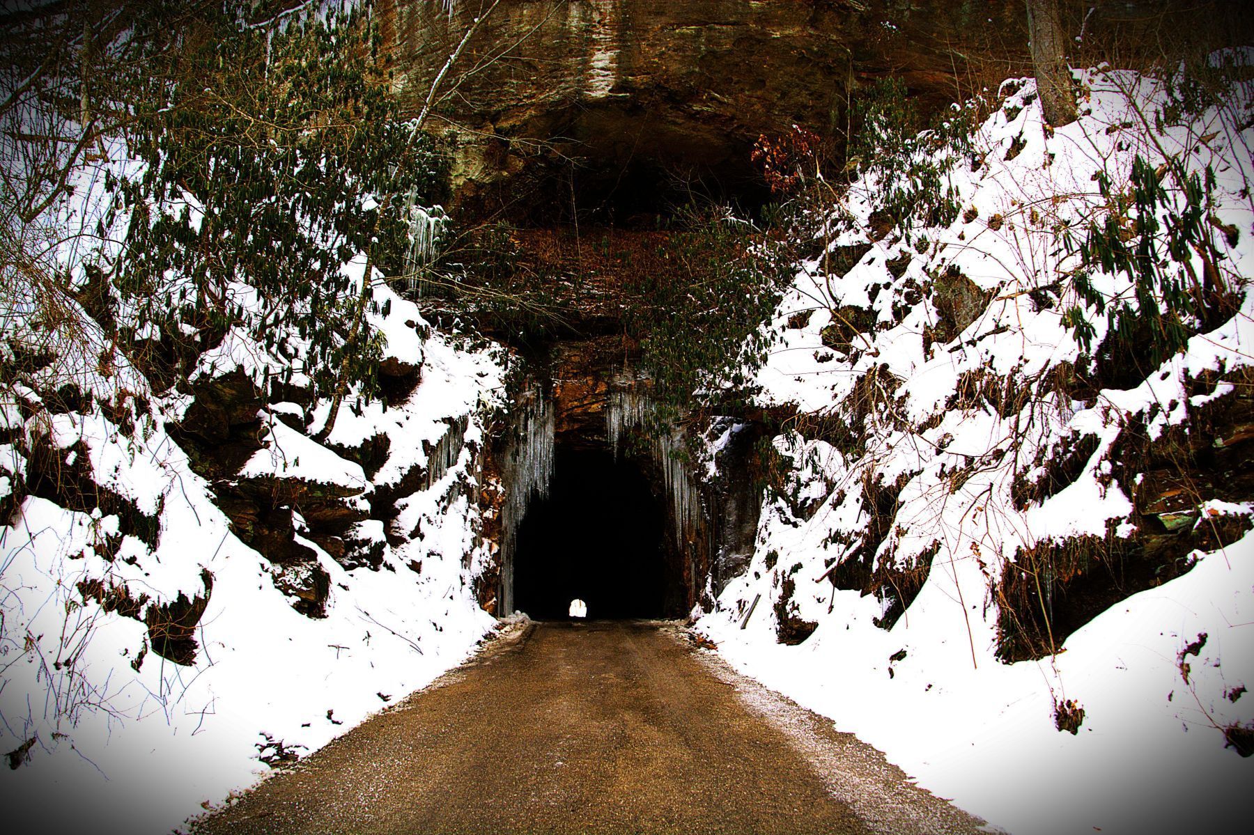 Tunnel entrance in snowy terrain with icicles.