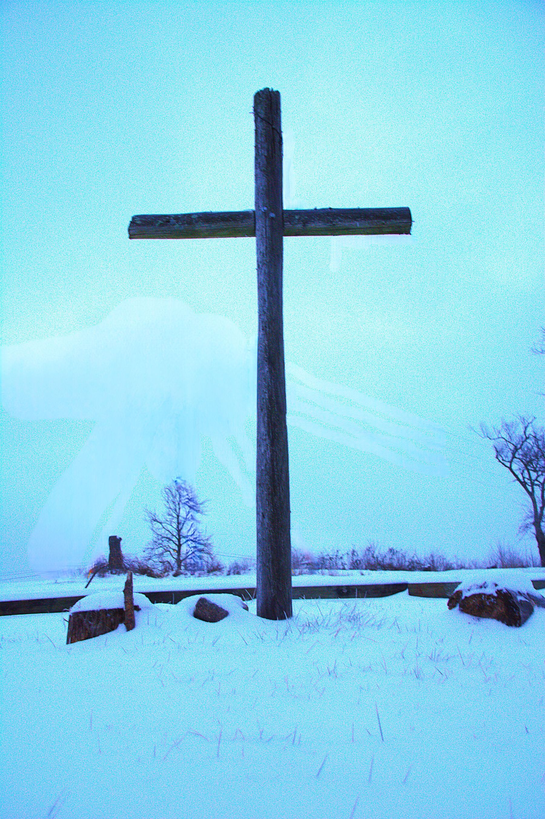 Wooden cross in snow-covered field under a blue sky.