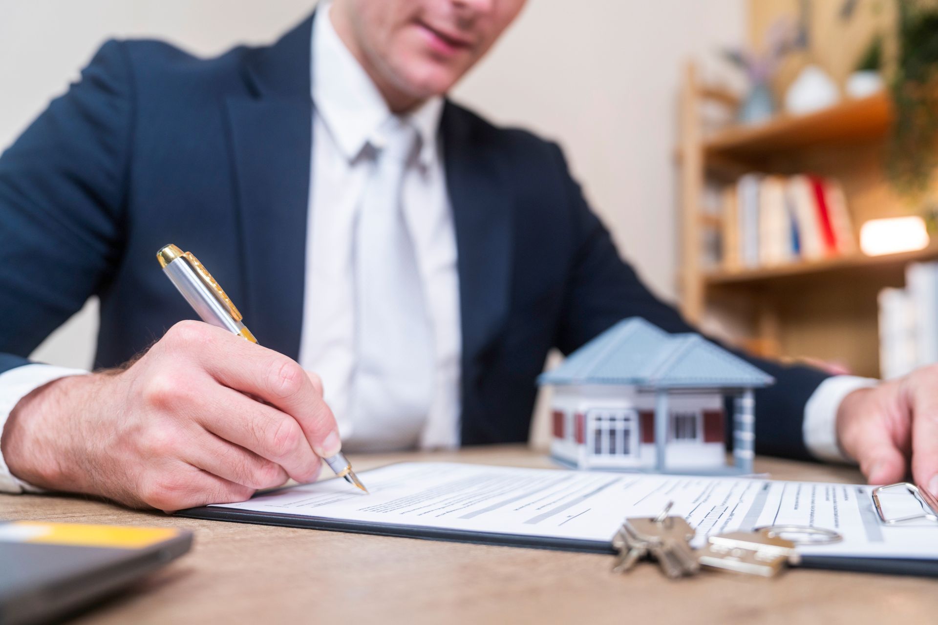 Estate attorney services expert filling out legal forms with pen near miniature house model on desk.