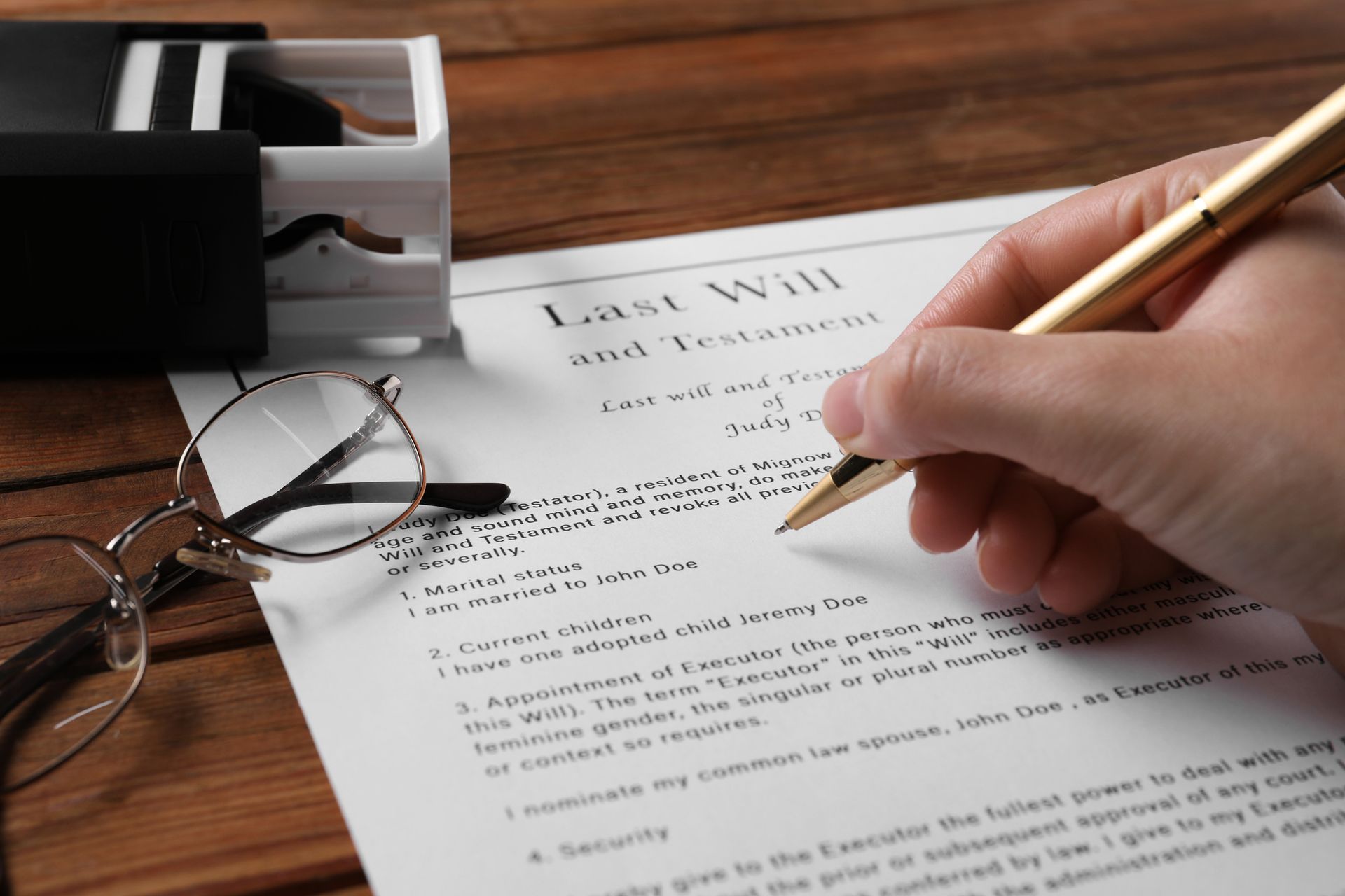 A close-up of a woman signing a Last Will and Testament at a wooden table.