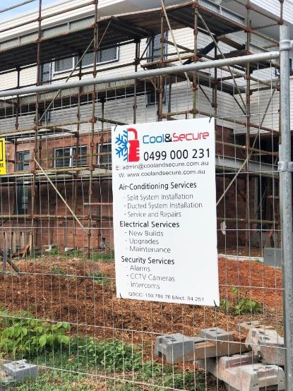 A Sign Is Hanging On A Fence In Front Of A Building Under Construction — Cool & Secure In Warana, QLD