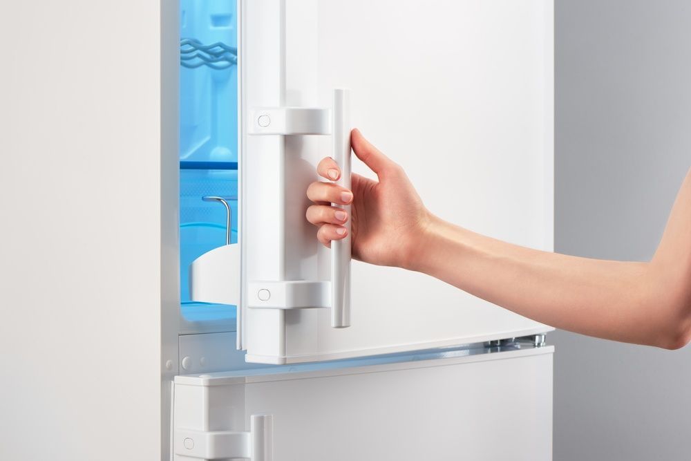 A Woman Is Opening The Door Of A White Refrigerator — Cool & Secure In Maroochydore, QLD