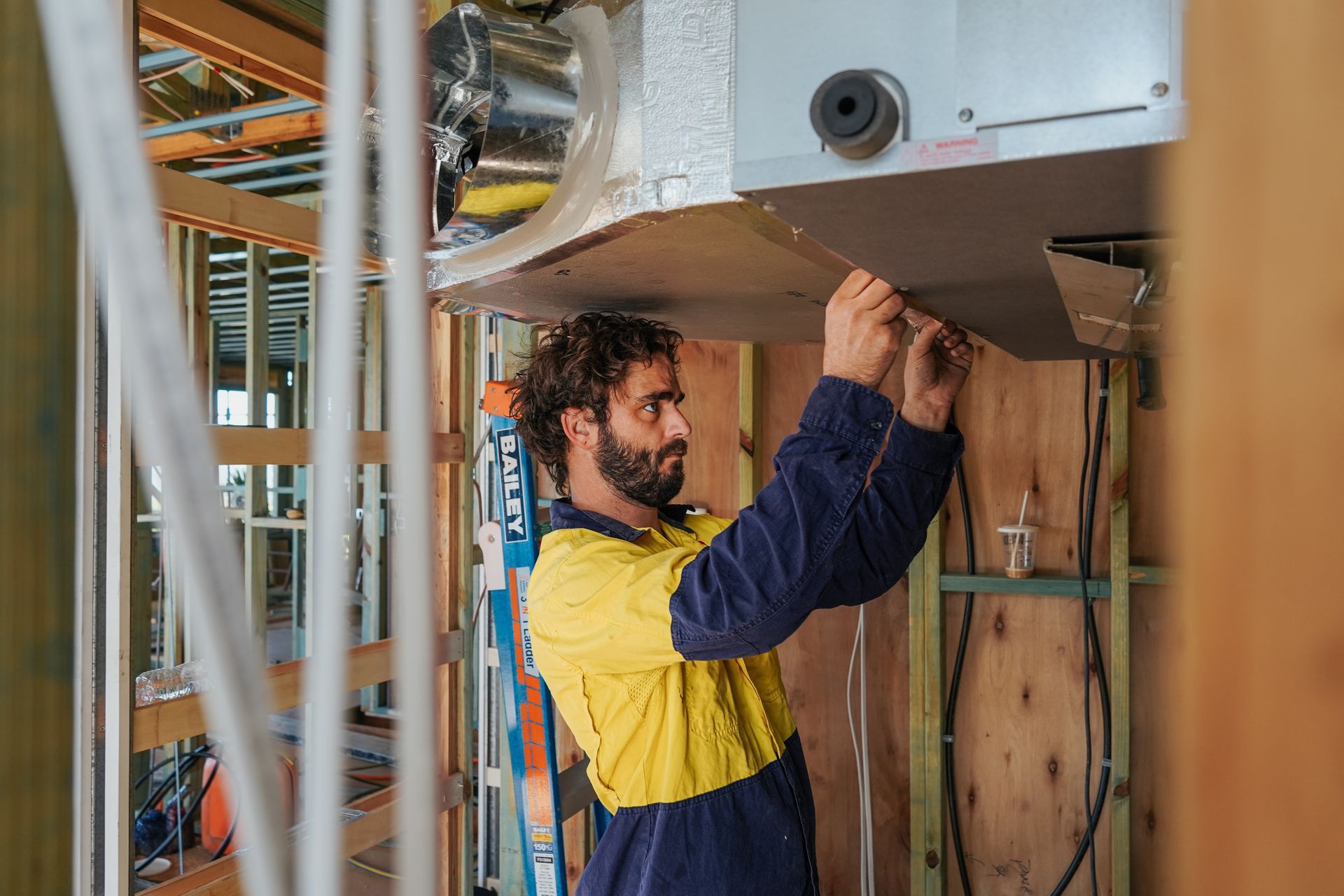 A Man In A Blue Shirt Is Working On An Air Conditioner — Cool & Secure In Maroochydore, QLD