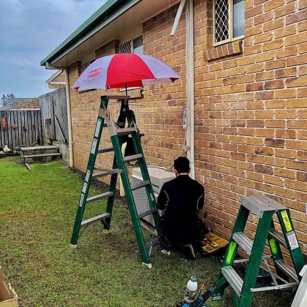 Person Working on an Air Conditioning Unit Outside a Brick House