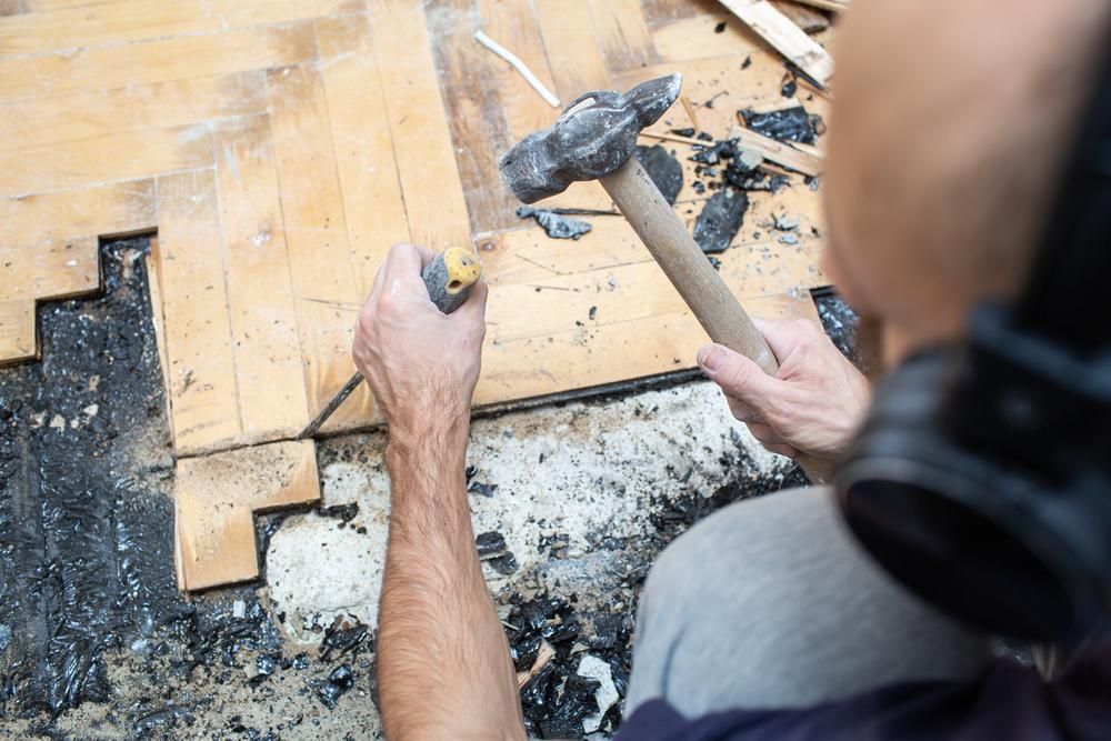A Man is Using a Hammer to Fix a Wooden Floor — Lennox Build In Alstonville, NSW
