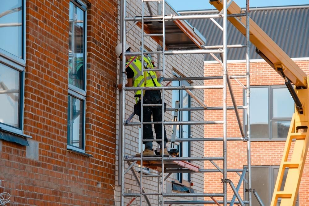 A Man is Standing on a Scaffolding Next to a Brick Building — Lennox Build In Evans Head, NSW