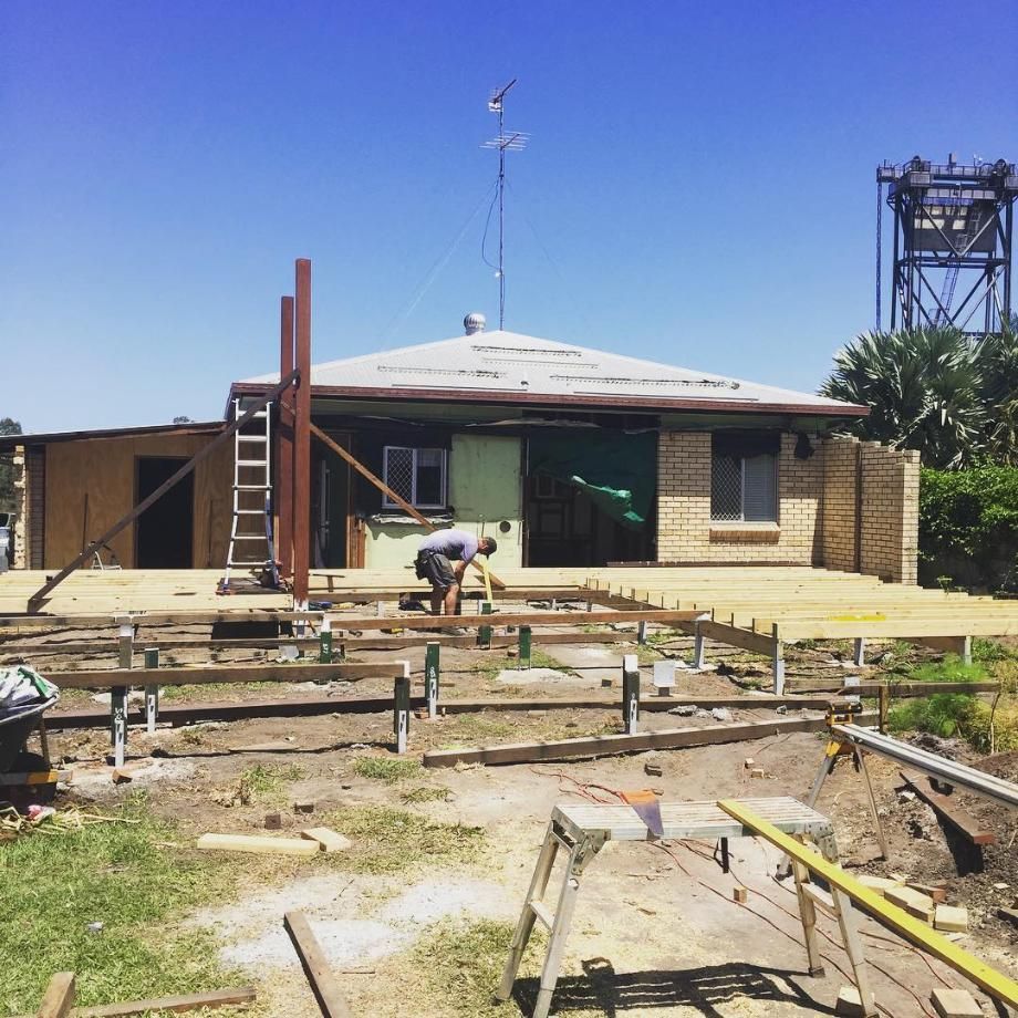 A Man is Working on a Wooden Deck in Front of a House — Lennox Build In Ballina, NSW