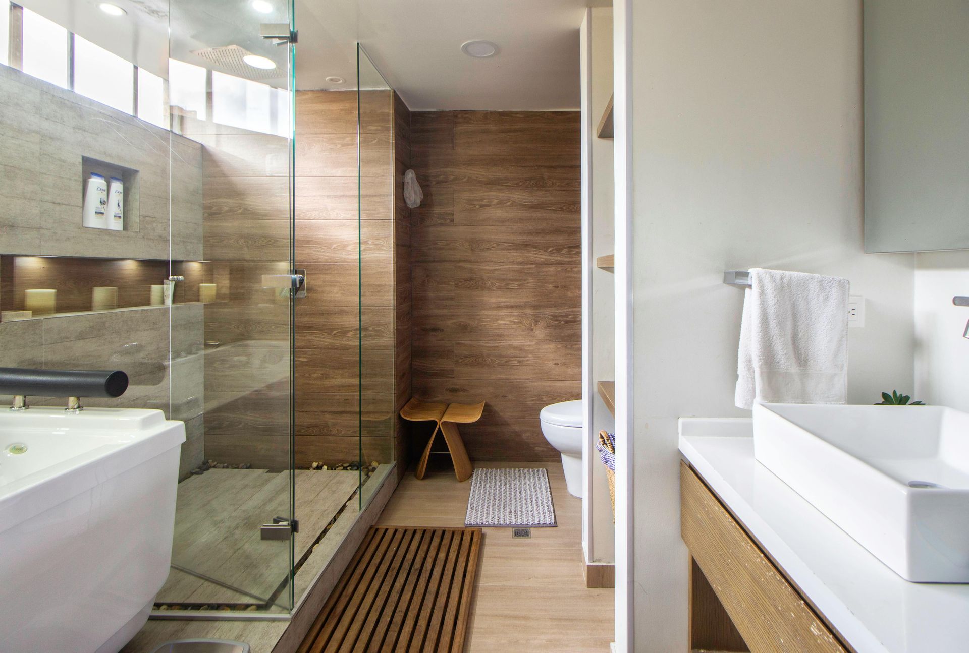 Modern bathroom with glass shower, soaking tub, wooden accents, and floating vanity.