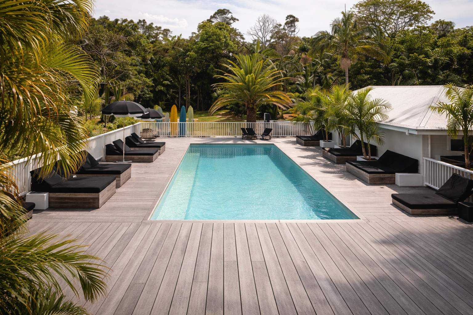 Pool with deck and lounge chairs in a tropical setting, trees and blue water.