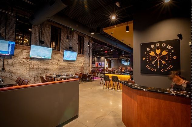 Interior of Arrow Dart Club, brick walls, bar, TVs, tables, and a sign.