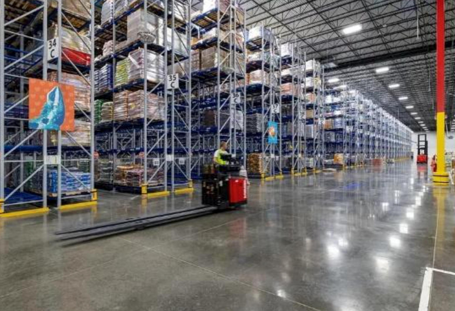 A man is driving a forklift in a large warehouse.