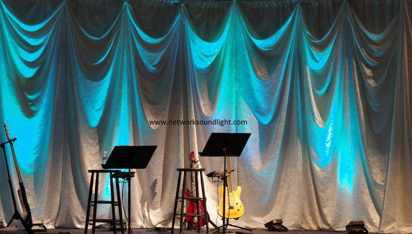 two guitars are sitting on a stage in front of a white curtain that says www.networksoundlight.com