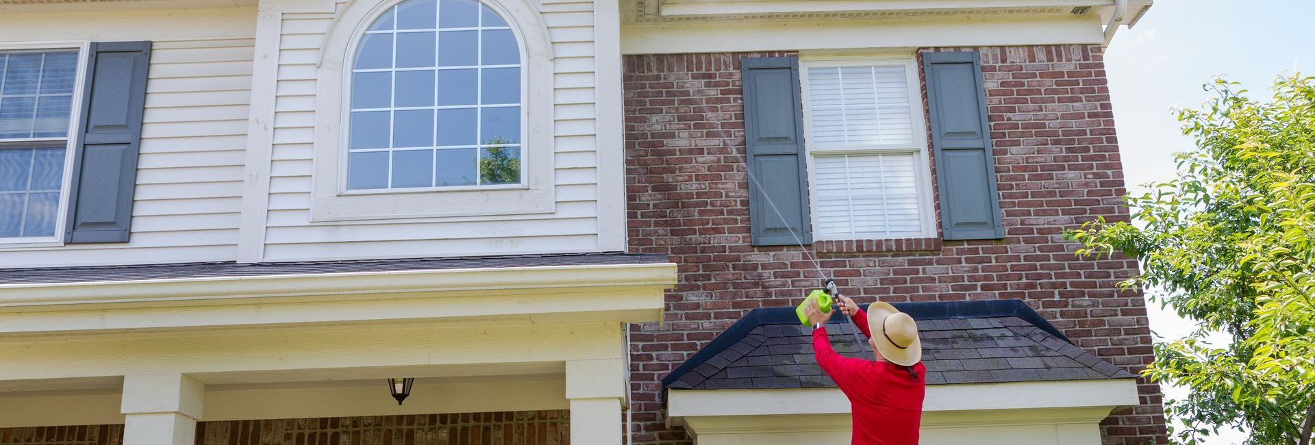 A woman is standing on a ladder painting a brick house.