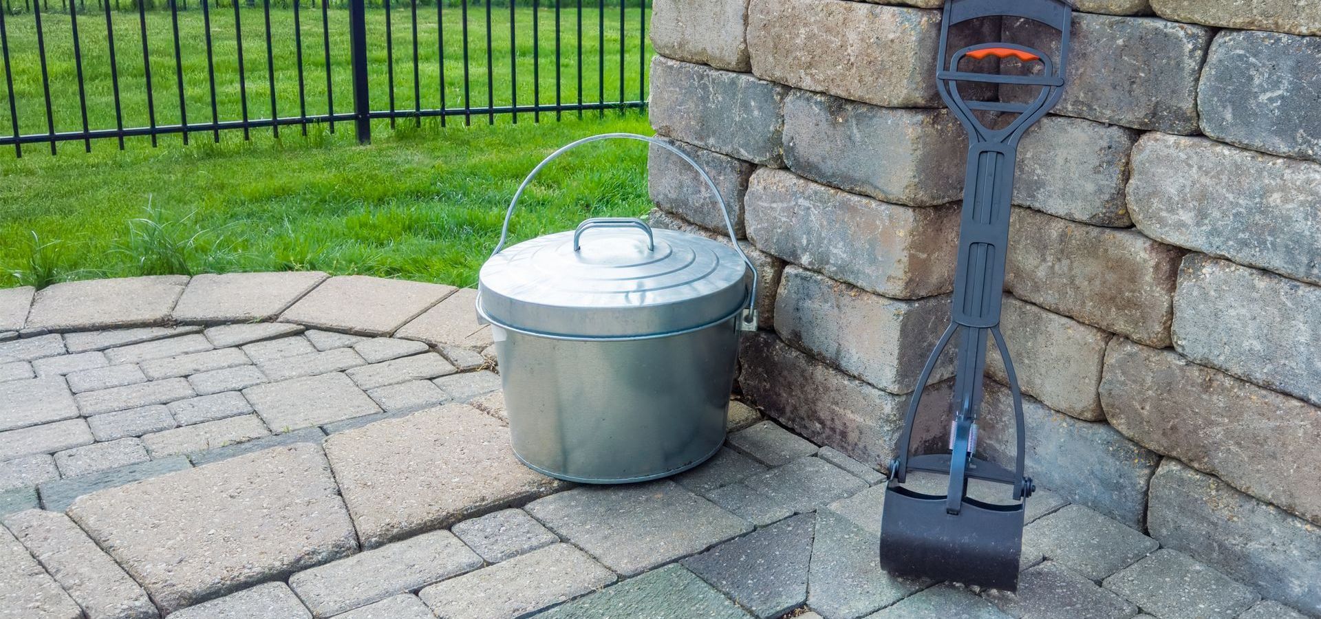 A bucket and a scoop are on a brick patio next to a brick wall.
